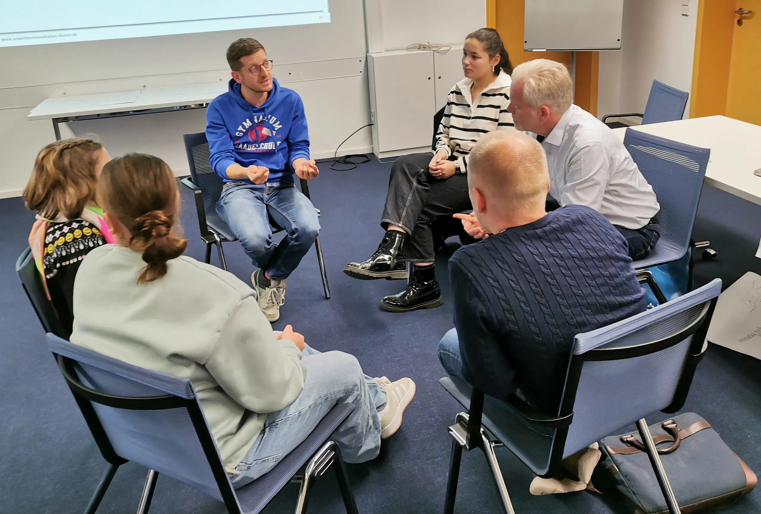 Erwachsene sitzen zusammen in einem Stuhlkreis und diskutieren.