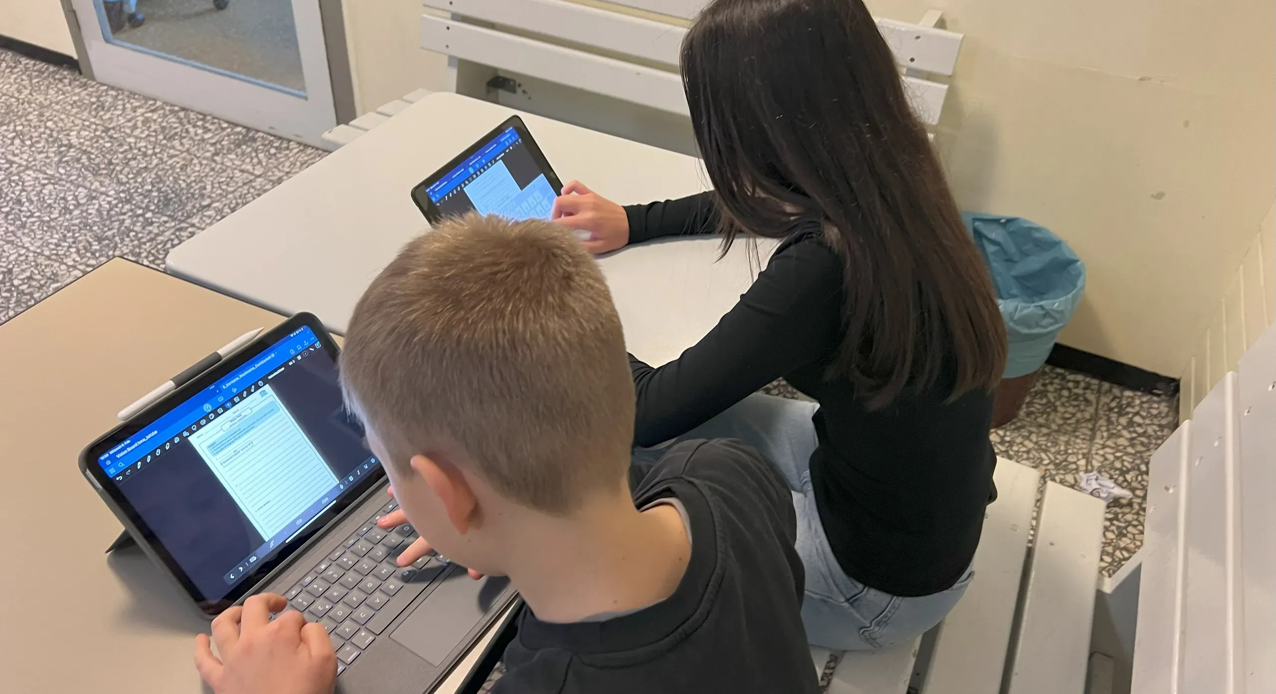 Zwei Kinder sitzen am Tisch und arbeiten an ihren Tablets.